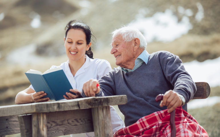 Smiling nurse reading book to senior man outdoor